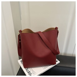 Detailed shot of burgundy bucket bag featuring a wide shoulder strap and gold rivets