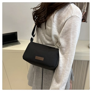 Détail d'un sac bandoulière en nylon noir avec écusson mode et bandoulière ajustable