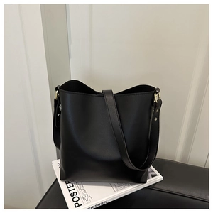 Detail view of smooth black bucket bag with wide shoulder strap and gold hardware accents