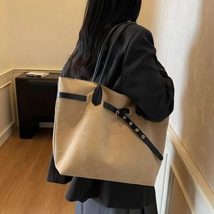 Grand sac cabas minimaliste en daim beige avec lanières en cuir noir porté par un mannequin