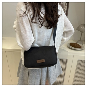 Vue détaillée d'un sac bandoulière en nylon noir avec écusson en cuir brun Fashion