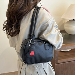 Modern black pebble leather crossbody bag with red heart charm on casual model