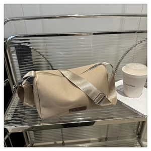 Détail du sac bandoulière beige avec large sangle en tissu et étiquette de mode décorative