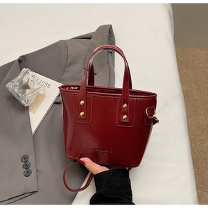 Detail of burgundy patent leather bucket bag with gold studs and brand lettering