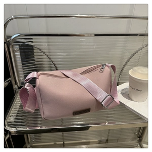 Détail d'un sac cylindrique rose avec étiquette en cuir marron et large bandoulière