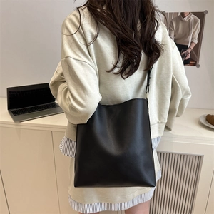 Minimalist black faux leather bucket bag with adjustable strap worn on the shoulder