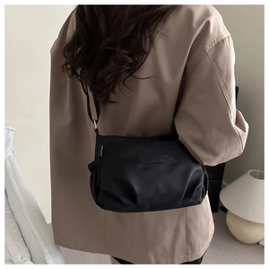 Close-up of a black nylon square crossbody bag showing textured fabric and side label