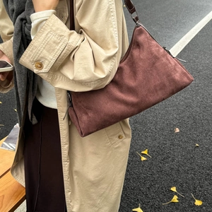Sac polochon minimaliste en daim marron porté à l'épaule dans un décor d'automne urbain