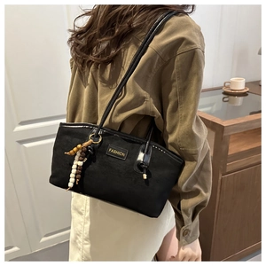 Detail of minimalist black suede tote bag featuring a boho beaded tassel and fashion label