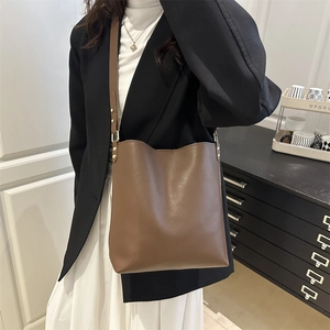 Minimalist brown leather bucket bag with gold hardware worn on a female shoulder
