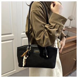 Detail of black suede tote bag with wooden bead charm and metal fashion plate