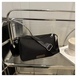 Gros plan du sac bandoulière en nylon noir avec écusson mode sur une étagère métallique