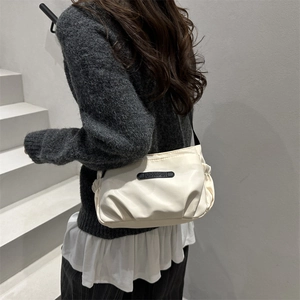 Minimalist beige crossbody bag with side ruching worn over a grey knit sweater