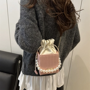 Pink woven bucket bag with pearl handle and chain strap worn over a shoulder