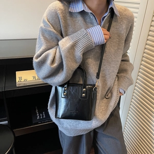 Chic black glossy leather bucket bag with gold rivets shown in a stylish daily outfit