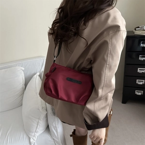Burgundy nylon crossbody bag with pleated design and black adjustable shoulder strap