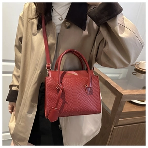 Detail of red snake-patterned leather crossbody bag worn with a stylish khaki coat