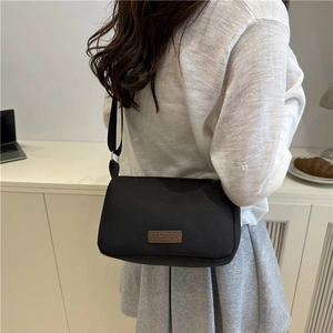 Sac bandoulière minimaliste en toile noire avec logo en cuir marron pour style décontracté
