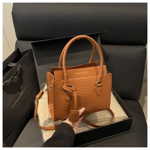 Close-up of brown crocodile embossed square bag with gold text in luxury gift box