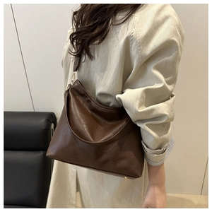 Détail d'un cabas en cuir marron foncé avec boucles dorées porté sur un trench-coat beige