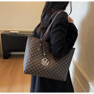 Detail of coffee brown tote bag featuring M-logo pattern and gold circular pendant