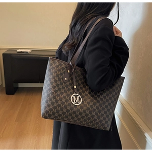 Macro detail of large dark brown tote bag with M letter jacquard and metal pendant charm