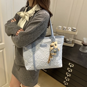 Sac fourre-tout bleu clair texturé avec breloque ours porté par un mannequin en intérieur