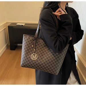 Detail of coffee tote bag with M-letter print and golden metallic charm on shoulder strap