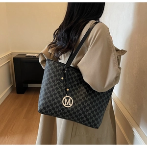 Detail of a large tote bag with M-letter prints and gold charm on a trench coat model