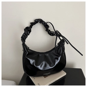 Detail of glossy black hobo bag featuring pleated handle and delicate side ribbon bow