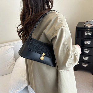 Sac sous le bras rétro en cuir noir avec rabat léopard et boucle dorée porté par un modèle