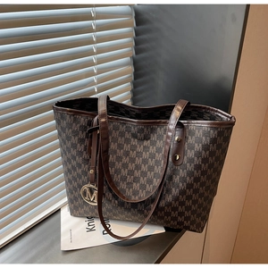 Close-up of monogram pattern tote bag with gold metal charm and leather handle detail