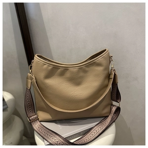 Détail du sac Hobo kaki avec large bandoulière ethnique posé sur des livres blancs