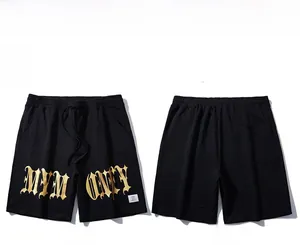 Detail of loose black sports shorts featuring gold gothic lettering and drawstring waist