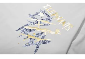 Détail de l'imprimé doré et des strass bleus sur un T-shirt blanc surdimensionné