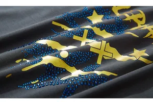 Gros plan d'un t-shirt gris foncé avec motif croix dorée et strass bleu brillant