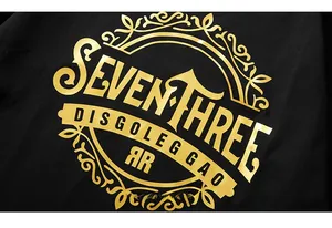 Dettaglio della scritta dorata Seven Three su t-shirt oversize in cotone nero
