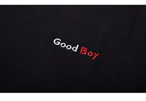 Detailed close-up of Good Boy embroidery in white and red on a black cotton T-shirt