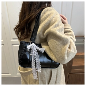 Close-up of sleek black underarm bag featuring a white lace bow detail on the side