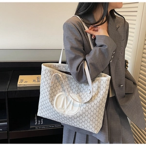 Detail of a large cream tote bag with grey monogram print and embossed M logo