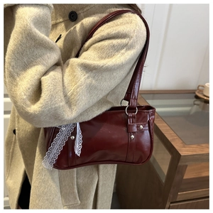 Dettaglio borsa a spalla bordeaux con pizzo bianco e borchie su cappotto beige