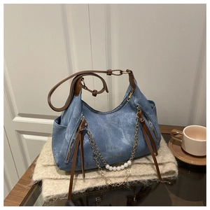 Détail du sac hobo en denim bleu avec lanières en cuir brun et chaîne perlée
