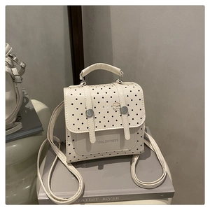 Detailansicht eines beigen Polka-Dot-Rucksacks mit Metallschnallen und Burger-Anhänger