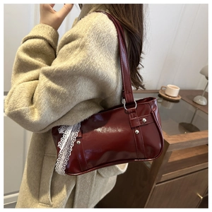 Detail of burgundy patent leather shoulder bag with white lace bow and rivet accents
