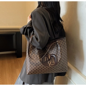 Detail of dark coffee monogram tote bag with M logo and long brown shoulder straps