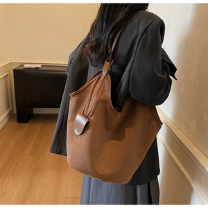 Detail of a large brown suede tote bag with leather trim on a shoulder in a room