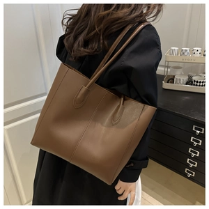 Detail view of large caramel brown leather tote bag worn over the shoulder by a model