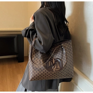Detail view of large brown tote bag with M-pattern print and embossed leather logo