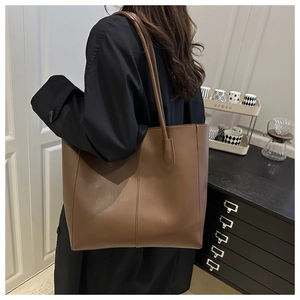 Detail of a brown leather tote bag with vertical stitching and slender shoulder straps