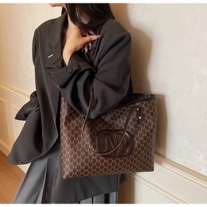 Detail of a large brown tote bag with M-letter pattern on a dark blazer outfit